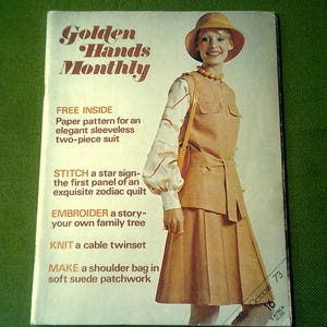 Könnte beinhalten: Ein Magazin-Cover für Golden Hands Monthly, das eine Frau in einem braunen, ärmellosen Kleid und einem breitkrempigen Hut zeigt. Der Covertext enthält "FREE INSIDE", "Paper pattern for an elegant sleeveless two-piece suit", "STITCH a star sign", "EMBROIDER a story", "KNIT a cable twinset", und "MAKE a shoulder bag in soft suede patchwork".
