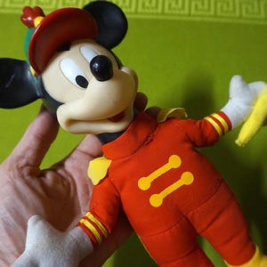 Puede incluir: Mu&ntilde;eco vintage de Mickey Mouse con uniforme de banda de m&uacute;sica rojo con detalles amarillos. El mu&ntilde;eco tiene orejas negras, gorro rojo y guantes blancos, sosteniendo una batuta amarilla. Un cl&aacute;sico de colecci&oacute;n de Disney.