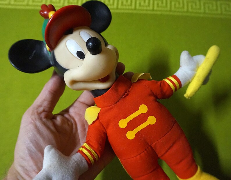Puede incluir: Mu&ntilde;eco vintage de Mickey Mouse con uniforme de banda de m&uacute;sica rojo con detalles amarillos. El mu&ntilde;eco tiene orejas negras, gorro rojo y guantes blancos, sosteniendo una batuta amarilla. Un cl&aacute;sico de colecci&oacute;n de Disney.