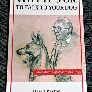May include: Book cover with a black and white illustration of a dog and a man wearing glasses. The title of the book is "Why It's OK To Talk To Your Dog" and the subtitle is "Co-evolution of People and Dogs". The author's name is David Paxton.
