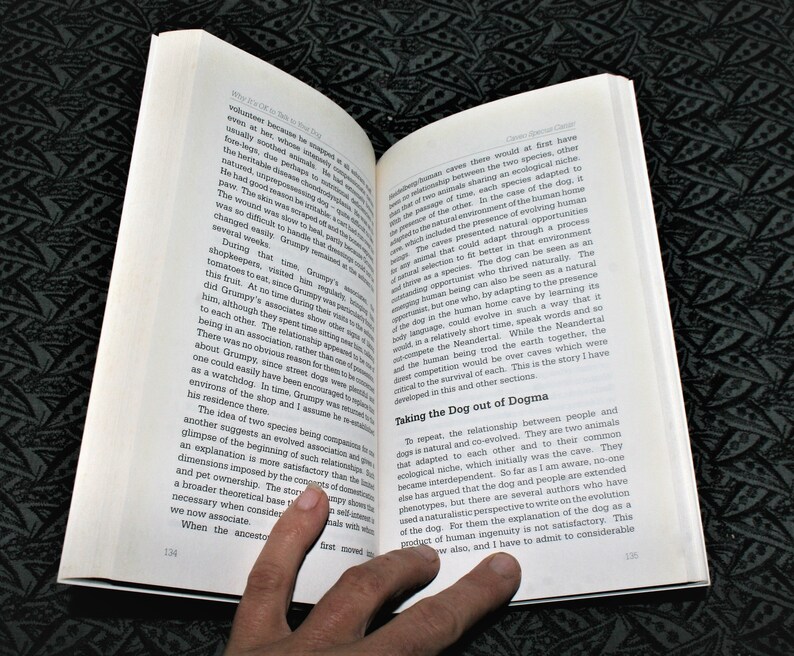 May include: A close-up of a book page with text about the relationship between humans and dogs. The text discusses the co-evolution of the two species and how they adapted to each other's environments. The book is open and the pages are slightly curled.
