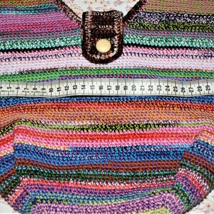 K&ouml;nnte beinhalten: Eine bunte gestreifte H&auml;keltasche mit einer braunen Lederklappe und einem Knopfverschluss. Die Tasche wird mit einem Ma&szlig;band gemessen, das eine Breite von 63,5 cm zeigt.