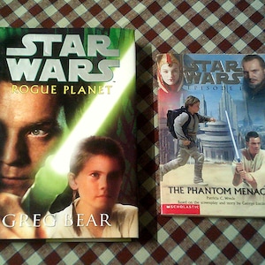 May include: Two Star Wars books are displayed. The first book, "Rogue Planet," features a close-up of a man holding a lightsaber. The second book, "Episode I The Phantom Menace," shows characters with lightsabers and futuristic buildings.