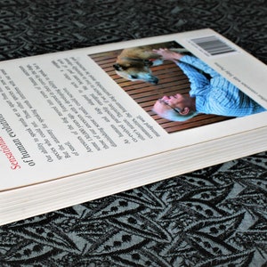 May include: The back cover of a book titled "Sensational...A profound re-appraisal of human evolution with dogs". The cover features a photo of a man petting a dog.