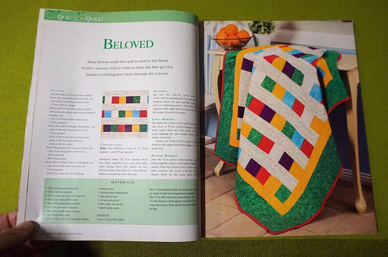 Puede incluir: Un edred&oacute;n colorido con un dise&ntilde;o geom&eacute;trico, con cuadrados rojos, azules, verdes y morados, sobre un fondo blanco. El edred&oacute;n est&aacute; bordeado con verde y amarillo. La palabra "Beloved" es visible en el libro abierto.