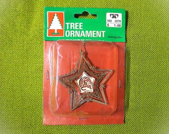 May include: A gold-coloured star-shaped Christmas tree ornament, displayed in a clear plastic package. The ornament features detailed cut-out patterns. The packaging is labelled with the words "TREE ORNAMENT" and a Christmas tree logo.