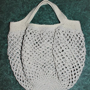 May include: A white crocheted tote bag with a wide, open top and a single handle. The bag is made of a delicate, open-weave pattern.