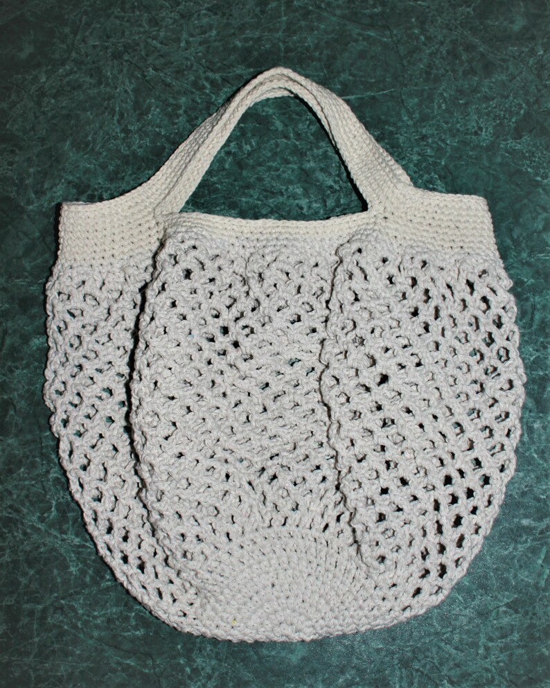 May include: A white crocheted tote bag with a wide, open top and a single handle. The bag is made of a delicate, open-weave pattern.