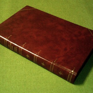 May include: A dark brown leather-bound book with gold accents and a title on the spine.