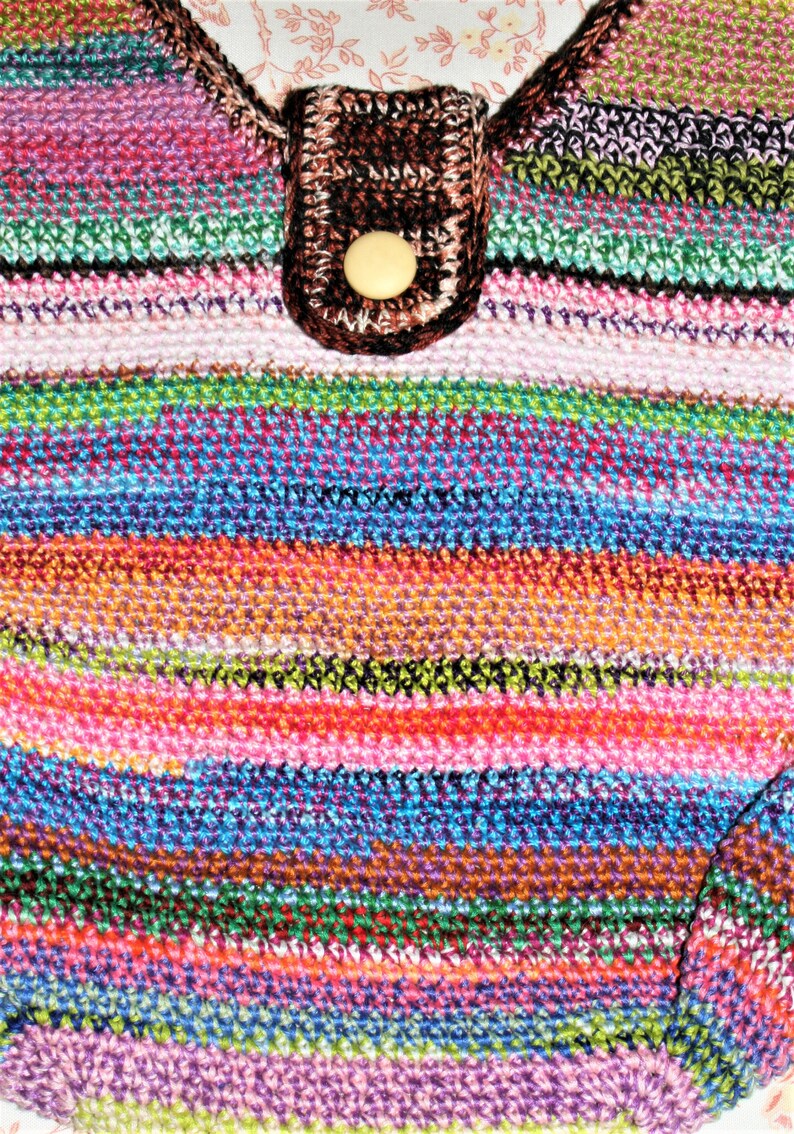 K&ouml;nnte beinhalten: Eine bunte gestreifte geh&auml;kelte Tasche mit einer braunen geh&auml;kelten Klappe und einem beigefarbenen Knopf.