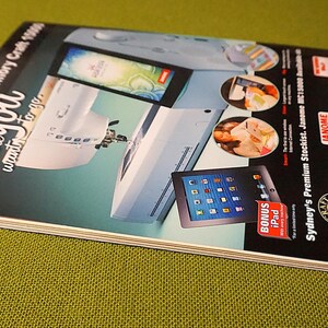 Puede incluir: Una revista con una portada turquesa y blanca que presenta una m&aacute;quina de coser, un iPad e im&aacute;genes de comida. El texto de la portada dice "The NEW Horizon Memory Craft 15000 Anywhere you want to go." Se anuncia un iPad de bonificaci&oacute;n.