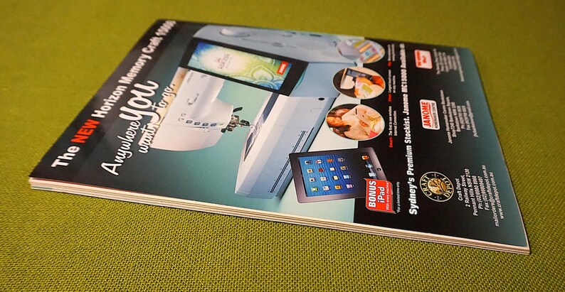 Puede incluir: Una revista con una portada turquesa y blanca que presenta una m&aacute;quina de coser, un iPad e im&aacute;genes de comida. El texto de la portada dice "The NEW Horizon Memory Craft 15000 Anywhere you want to go." Se anuncia un iPad de bonificaci&oacute;n.