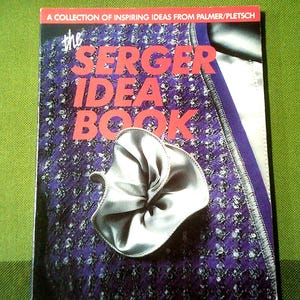 May include: The Serger Idea Book, a collection of inspiring ideas from Palmer/Pletsch, features a purple and white fabric with a silver bow.