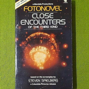 May include: A vintage paperback book titled "Fotonovel: Close Encounters of the Third Kind" with a dark cover featuring a glowing orange and yellow image of a spacecraft. The book is based on the screenplay by Steven Spielberg.