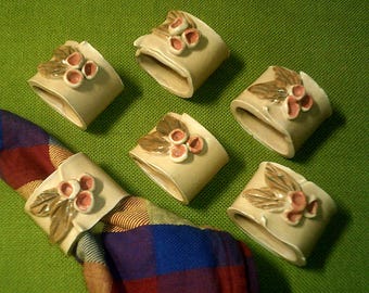 May include: Six ceramic napkin rings with a floral design. Each ring features a cluster of pink flowers with brown leaves.