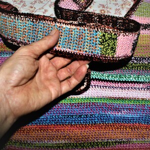 K&ouml;nnte beinhalten: Eine bunte gestreifte H&auml;keltasche mit einem passenden H&auml;kelriemen. Die Tasche ist aus verschiedenen Farben gefertigt, darunter Pink, Gr&uuml;n, Blau und Orange.