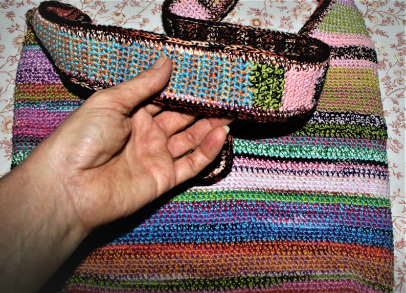 K&ouml;nnte beinhalten: Eine bunte gestreifte H&auml;keltasche mit einem passenden H&auml;kelriemen. Die Tasche ist aus verschiedenen Farben gefertigt, darunter Pink, Gr&uuml;n, Blau und Orange.