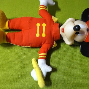 Puede incluir: Un peluche vintage de Mickey Mouse con un atuendo rojo con detalles amarillos, guantes blancos y zapatos amarillos. El n&uacute;mero "11" est&aacute; en el pecho. El juguete tiene orejas negras, un sombrero rojo y una cara blanca.