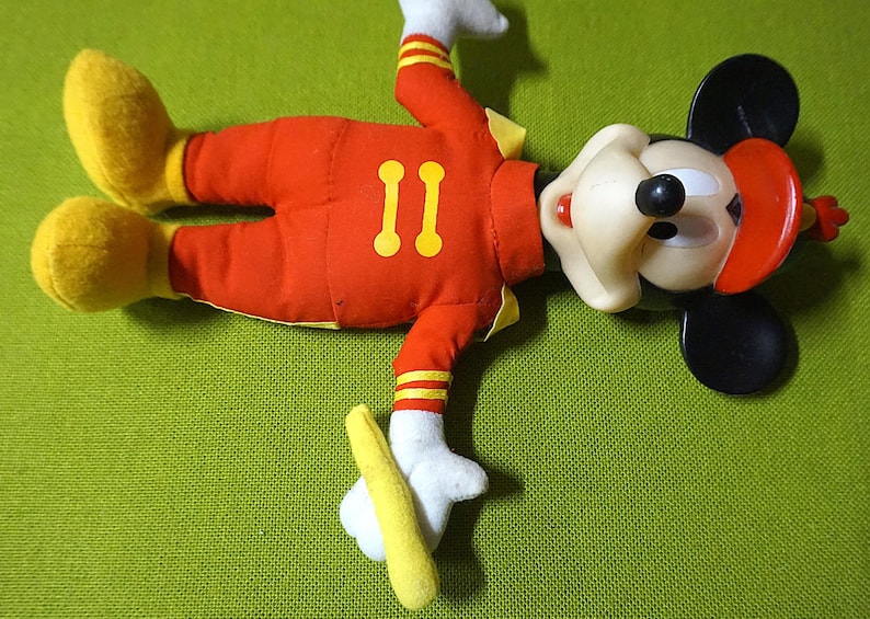 Puede incluir: Un peluche vintage de Mickey Mouse con un atuendo rojo con detalles amarillos, guantes blancos y zapatos amarillos. El n&uacute;mero "11" est&aacute; en el pecho. El juguete tiene orejas negras, un sombrero rojo y una cara blanca.