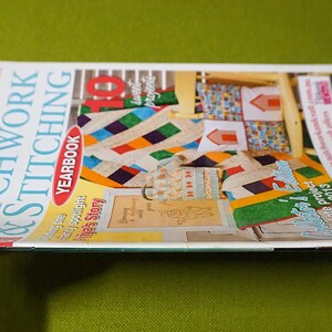 Puede incluir: Una revista titulada "Patchwork & Stitching Yearbook" se sostiene en una mano. La portada presenta coloridos dise&ntilde;os de edredones y el texto "10 Complete Projects". El fondo es de color verde liso.