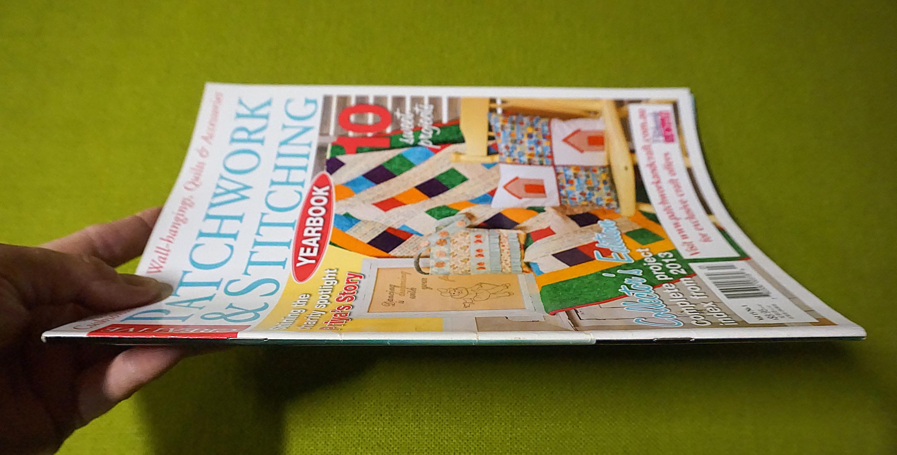 Puede incluir: Una revista titulada "Patchwork & Stitching Yearbook" se sostiene en una mano. La portada presenta coloridos dise&ntilde;os de edredones y el texto "10 Complete Projects". El fondo es de color verde liso.
