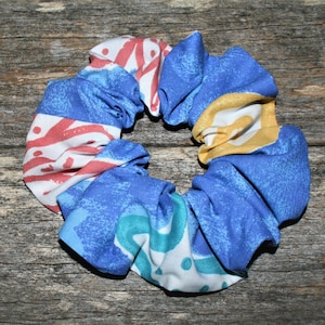 Puede incluir: Un scrunchie con estampado azul, rojo, blanco y amarillo. El scrunchie está hecho de tela y está anudado.