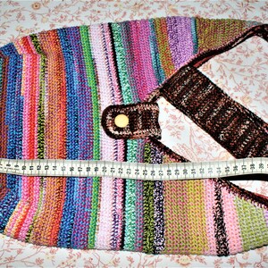 K&ouml;nnte beinhalten: Eine bunte gestreifte geh&auml;kelte Tragetasche mit einem braunen Ledergriff und einem goldenen Knopf. Die Tasche ist 119 cm lang.