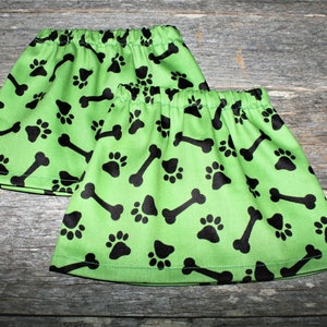 Może przedstawiać: Dwa zielone ocieplacze na nogi z czarnym wzorem łap i kości.