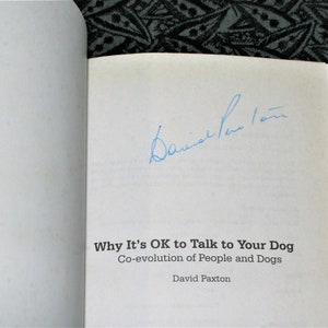 May include: A white book with the title "Why It's OK to Talk to Your Dog" and the subtitle "Co-evolution of People and Dogs" by David Paxton. The book is signed by the author.