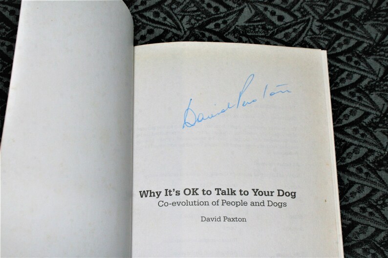 May include: A white book with the title "Why It's OK to Talk to Your Dog" and the subtitle "Co-evolution of People and Dogs" by David Paxton. The book is signed by the author.
