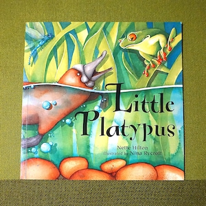 May include: A children's book cover for "Little Platypus", featuring a platypus, frog, and dragonfly in a pond. The artwork is colourful, with the title in large letters and the author and illustrator's names.