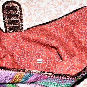 K&ouml;nnte beinhalten: Eine bunte geh&auml;kelte Tasche mit roter und wei&szlig;er Blumenfutter. Die Tasche hat einen braunen geh&auml;kelten Griff.