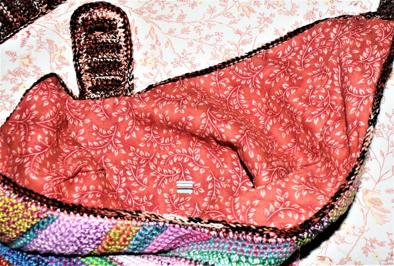 K&ouml;nnte beinhalten: Eine bunte geh&auml;kelte Tasche mit roter und wei&szlig;er Blumenfutter. Die Tasche hat einen braunen geh&auml;kelten Griff.