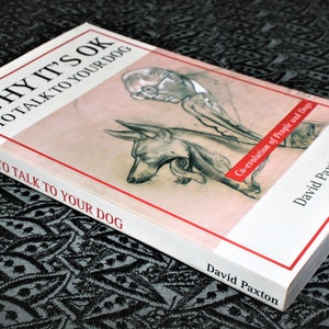 May include: A white book titled "Why It's OK to Talk to Your Dog" with a red stripe and a black and white illustration of a person and a dog on the cover. The book's subtitle is "Co-evolution of People and Dogs". The author's name, David Paxton, is printed on the spine and bottom of the book.