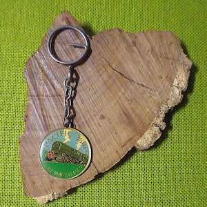 May include: A vintage Pacific Limited train keychain with a circular pendant. The pendant features a green train with the text "Pacific Limited" and "Keep Our Steam". The keychain is attached to a silver chain and ring.