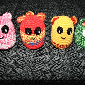 Peut inclure: Quatre jouets en peluche crochetés en forme d'animaux. Les jouets sont rose, rouge, jaune et vert. Chaque jouet a une expression faciale et des caractéristiques différentes.