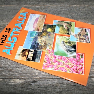Può includere: Un libretto arancione con il testo "This is Australia" sulla copertina. La copertina presenta un collage di immagini colorate di monumenti e paesaggi australiani.