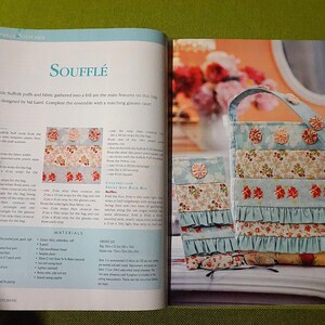 Puede incluir: Libro abierto con el t&iacute;tulo "Souffl&eacute;" y un tutorial para una bolsa de tela con detalles florales y volantes. La bolsa es azul claro con detalles florales y rojos. El libro est&aacute; abierto sobre una superficie verde.