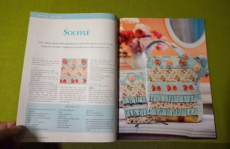 Puede incluir: Libro abierto con el t&iacute;tulo "Souffl&eacute;" y un tutorial para una bolsa de tela con detalles florales y volantes. La bolsa es azul claro con detalles florales y rojos. El libro est&aacute; abierto sobre una superficie verde.