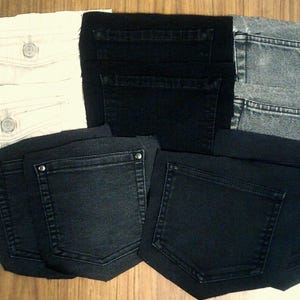 May include: A selection of denim jeans in shades of black, grey, and off-white. The jeans are displayed with their pockets facing upwards, revealing the different styles and washes. The image showcases the variety of denim options available.