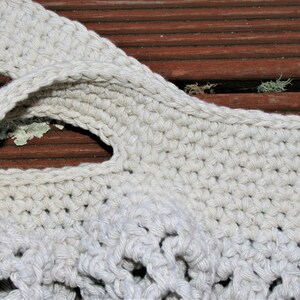 May include: Close-up of a crocheted tote bag with a cream-colored yarn. The bag has a wide, flat handle and a woven design.