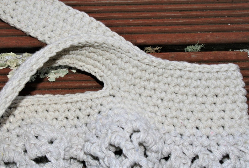 May include: Close-up of a crocheted tote bag with a cream-colored yarn. The bag has a wide, flat handle and a woven design.