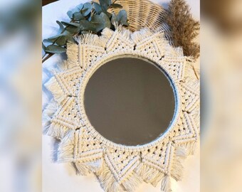 May include: A white macrame mirror with a round mirror in the center. The mirror is surrounded by a fringe of white yarn.