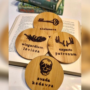 Könnte beinhalten: Vier runde Holz-Untersetzer mit Harry-Potter-Motiven. Die Zauberformeln sind "Wingardium Leviosa", "Alohomora", "Expecto Patronum" und "Avada Kedavra".
