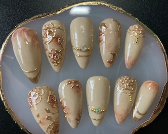 May include: Set of ten beige false nails with gold floral designs and rhinestones.