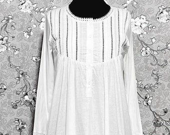 Peut inclure: Une chemise de nuit en coton blanc à manches longues et à fermeture boutonnée sur le devant. L'encolure et les manches sont ornées de bordures noires et d'une bordure en dentelle blanche.