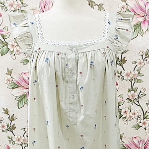 May include: A light sage green nightgown featuring a square neckline with white lace trim, flutter sleeves, and a button-down placket. The fabric is decorated with a small, repeating pattern of blue and red palm trees, finished with a ruffled hem.