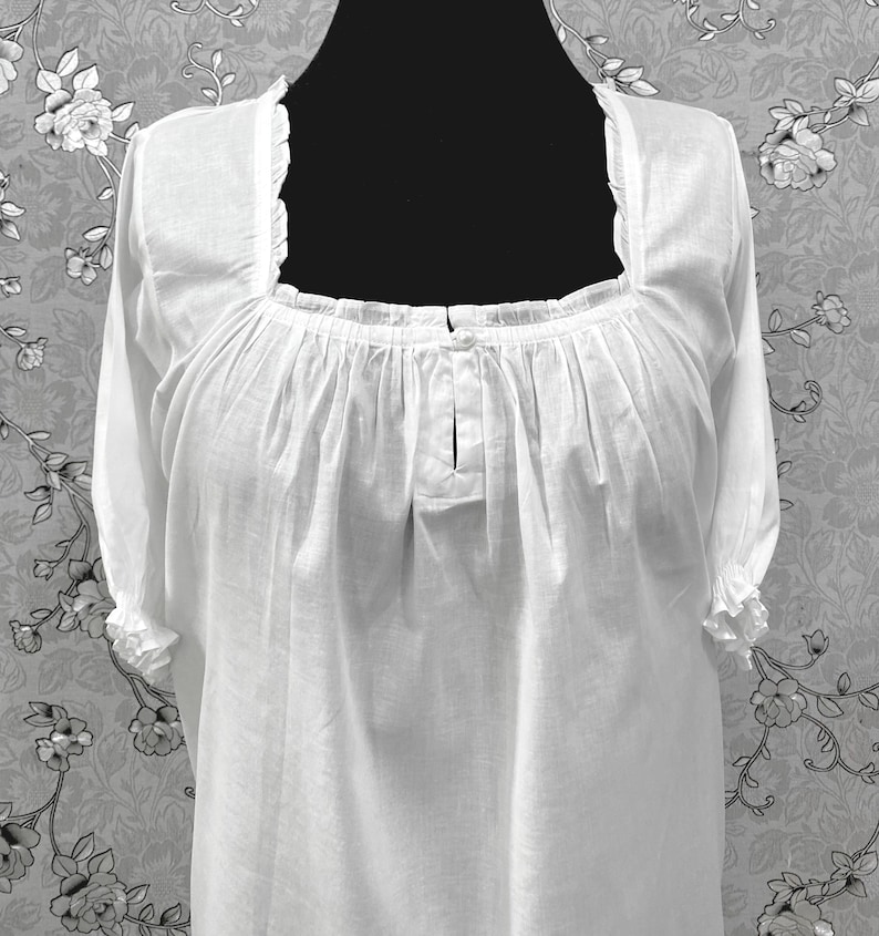 May include: A white, long-sleeved blouse with a square neckline and ruffled trim. The blouse features gathered fabric details at the neckline and sleeves. The garment is displayed on a black mannequin.