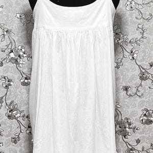 Peut inclure: Robe de nuit blanche en coton avec une bordure en dentelle autour de l'encolure et de l'ourlet. La robe a un corsage pliss&eacute; et une jupe ample.