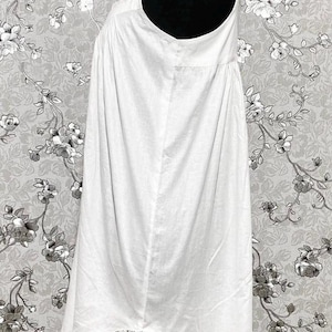 Peut inclure: Une robe de nuit blanche en coton avec une bordure en dentelle &agrave; l'ourlet. La robe est sans manches et a un col rond.